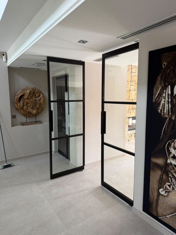 Dos puertas pivotantes de acero negro y cristal con tres paneles