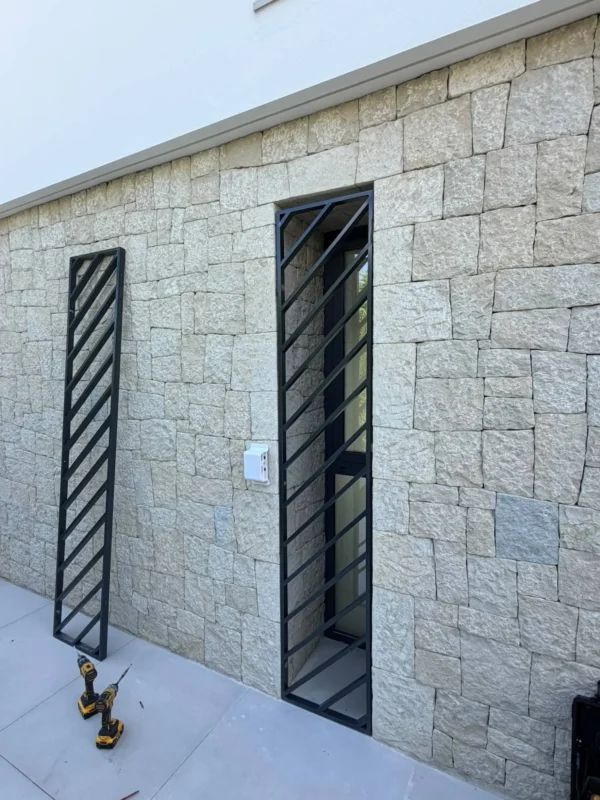 Reja de acero negro con barras diagonales instalada en una ventana de fachada de piedra