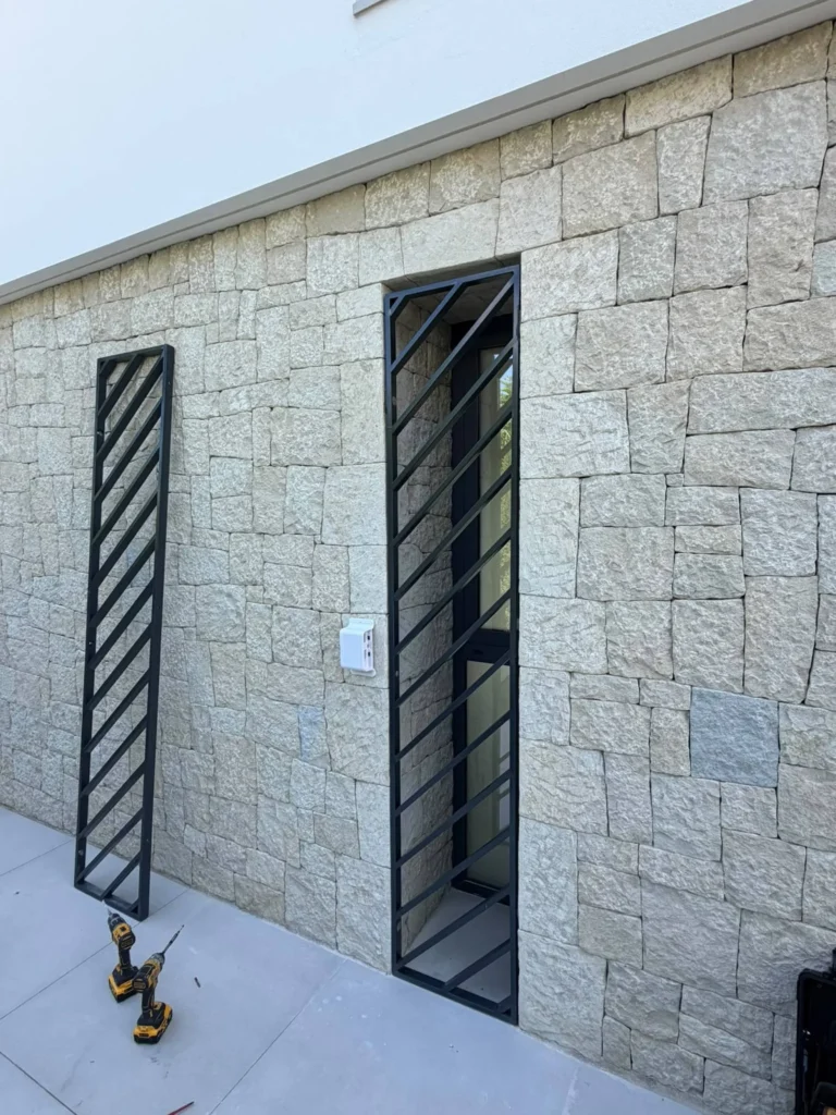 Reja de acero negro con barras diagonales instalada en una ventana de fachada de piedra