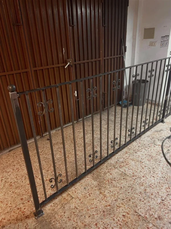 Reja de forja negra con barrotes y volutas hecha a medida